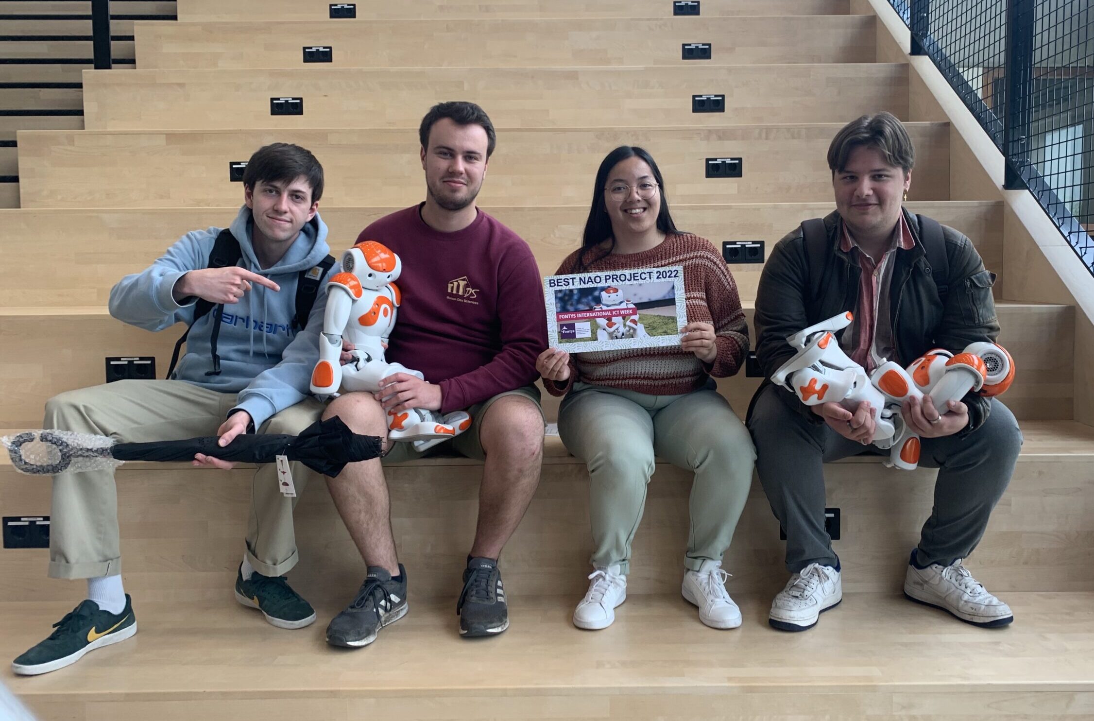 Group sitting on flight of stairs posing with robot