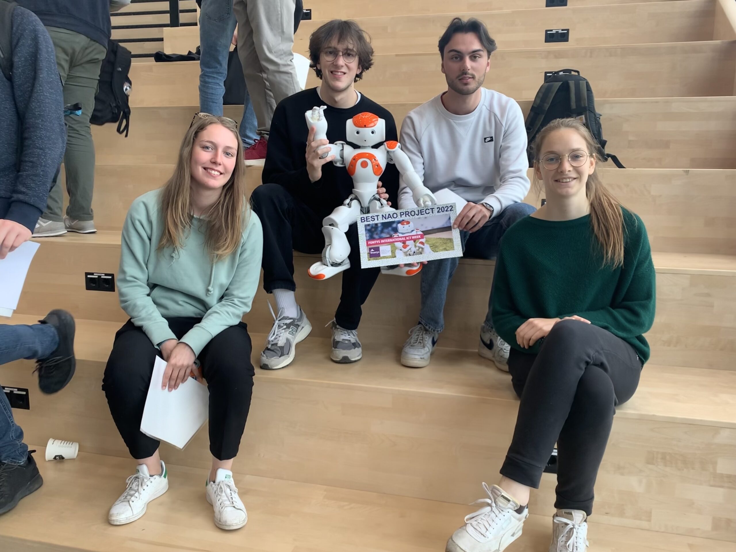 Group sitting on flight of stairs posing with robot